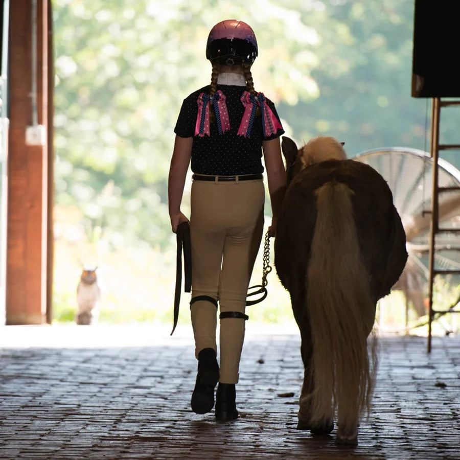 Niña con casco Troxel Spirit Skydream caminando junto a un pony al aire libre