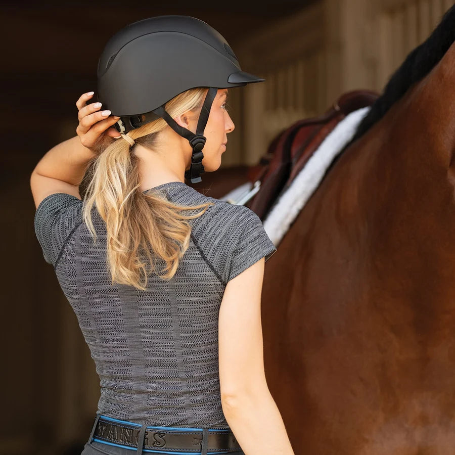 Amazona de espaldas con casco Troxel Liberty negro Duratec junto a su caballo