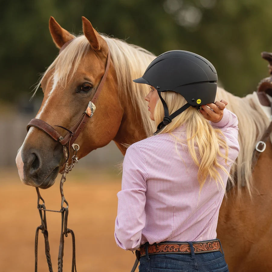 Amazona con casco Troxel Spirit MIPS negro junto a la cabeza de un caballo palomino