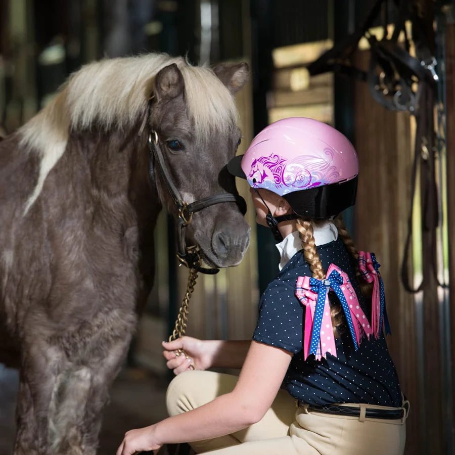 Niña con casco Troxel Spirit Skydream rosa acariciando a un pony gris
