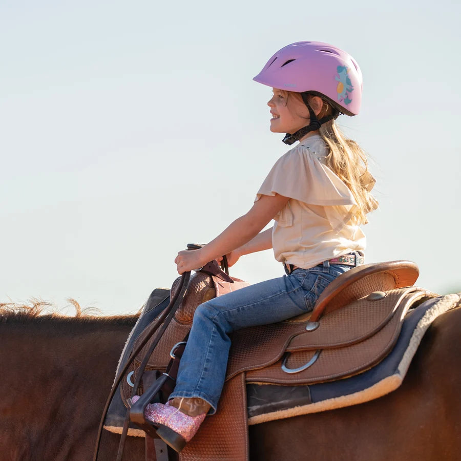 Niña con casco Troxel Youngster lila montando a caballo al atardecer