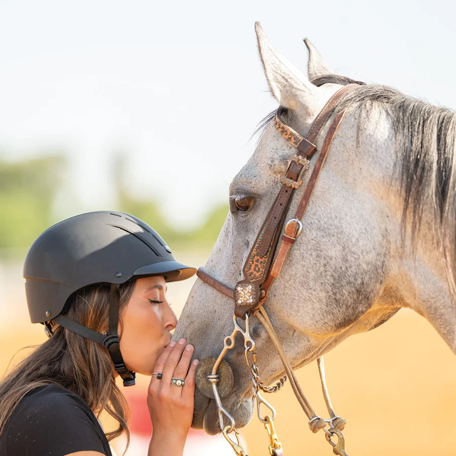 Amazona con casco Troxel Spirit negro acariciando a un caballo tordo