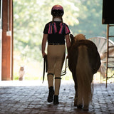 Niña con casco Troxel Spirit Skydream caminando junto a un pony al aire libre