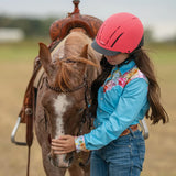 Niña con casco Troxel Spirit MIPS rosa fucsia abrazando a su caballo