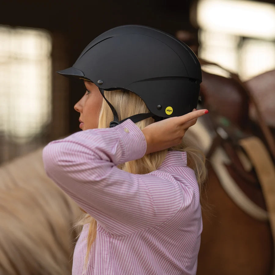 Amazona ajustándose el casco Troxel Spirit MIPS negro junto a su caballo