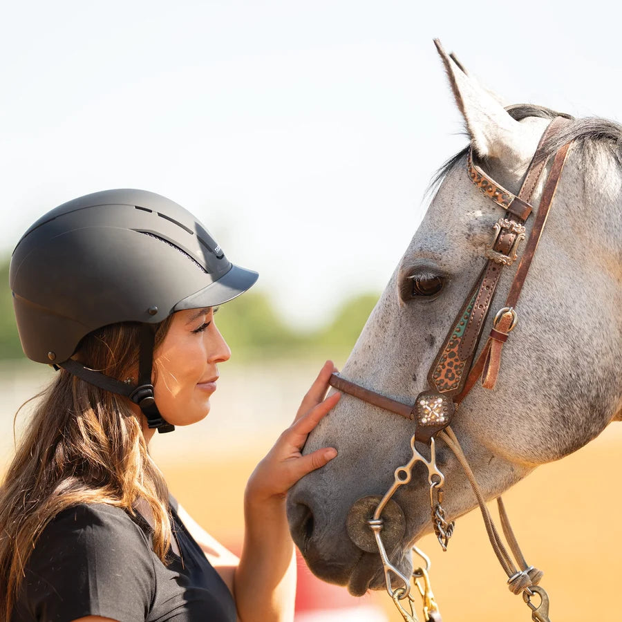 Amazona con casco Troxel Spirit negro junto a un caballo tordo