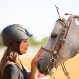 Amazona con casco Troxel Spirit negro junto a un caballo tordo
