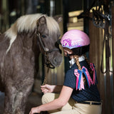 Niña con casco Troxel Spirit Skydream rosa acariciando a un pony gris