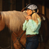Amazona con camisa verde menta y casco Troxel Spirit MIPS abrazando a un caballo palomino