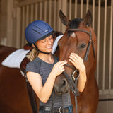 Niña con casco Troxel Spirit azul marino junto a dos caballos en el establo