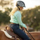 Amazona con camisa verde menta y casco Troxel Spirit MIPS montando a caballo