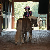 Niña con casco Troxel Spirit Skydream rosa junto a un pony en el establo